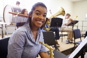 Female Pupil Playing Saxophone In High School Orchestra